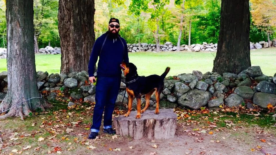 Nick Messina standing beside a dog on a tree stump outdoors